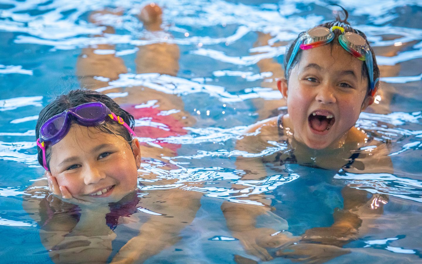 Two smiling girls playing in the toddler pool wearing goggles at the Christchurch Recreation and Sport pool. 