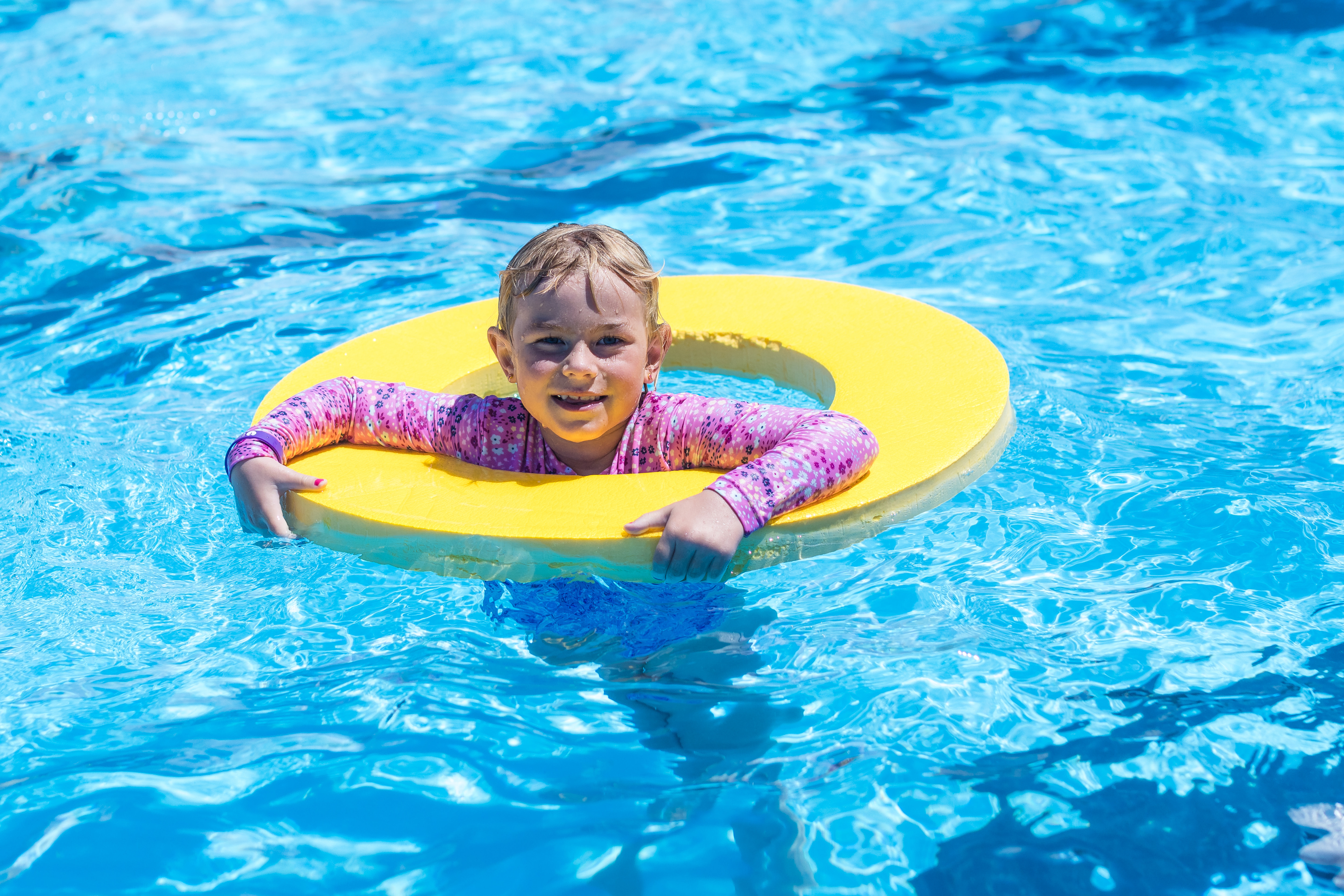 A smiling girl holding onto a yellow flotation ring at the Halswell Summer pool. 
