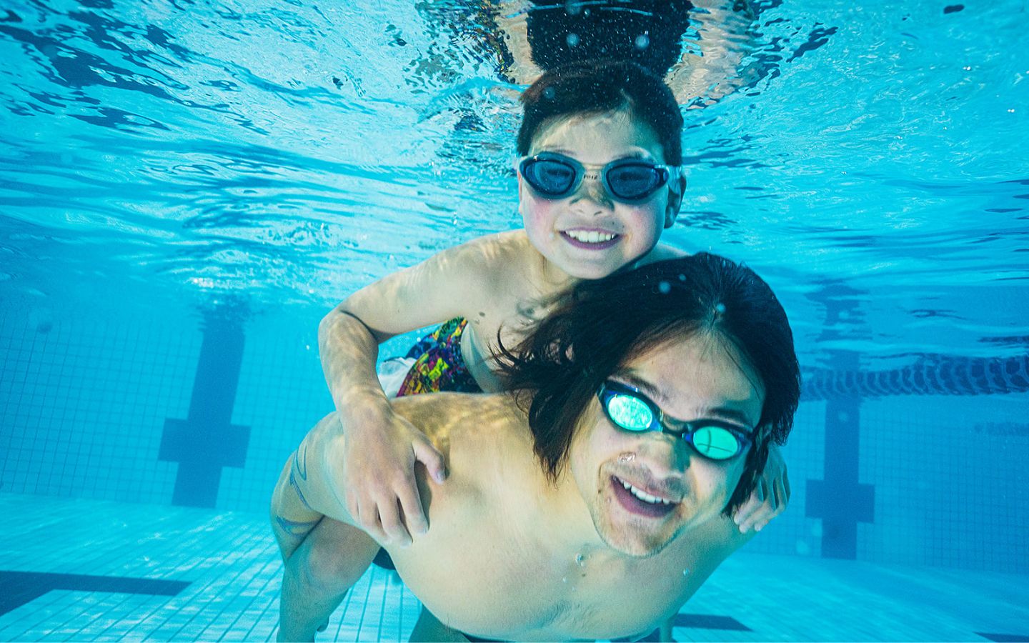Two boys wearing goggles smiling underwater at a Christchurch outdoor summer pool. 
