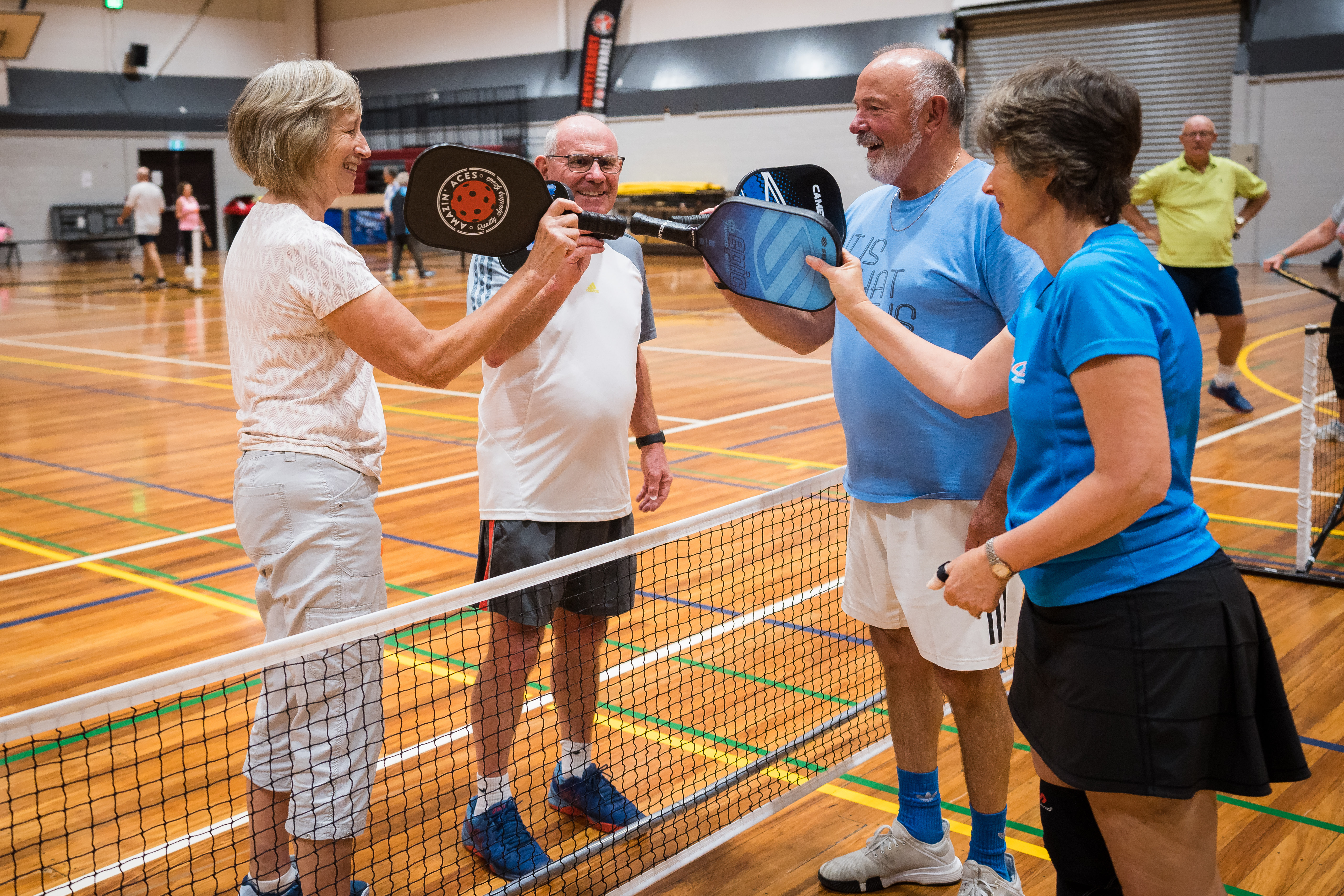 Two women and two men playing doubles pickleball high-fiving paddles at Christchurch Recreation and Sport centre. 