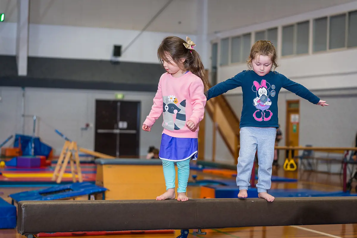 Two girls balancing on a balance beam during a Tumbletimes class at Christchurch Recreation and Sport Centre.