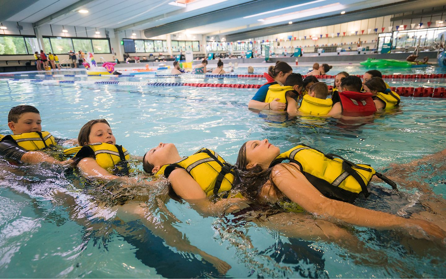 A group of children in yellow lifejackets laying in a line at Christchurch Recreation and Sport pool. 