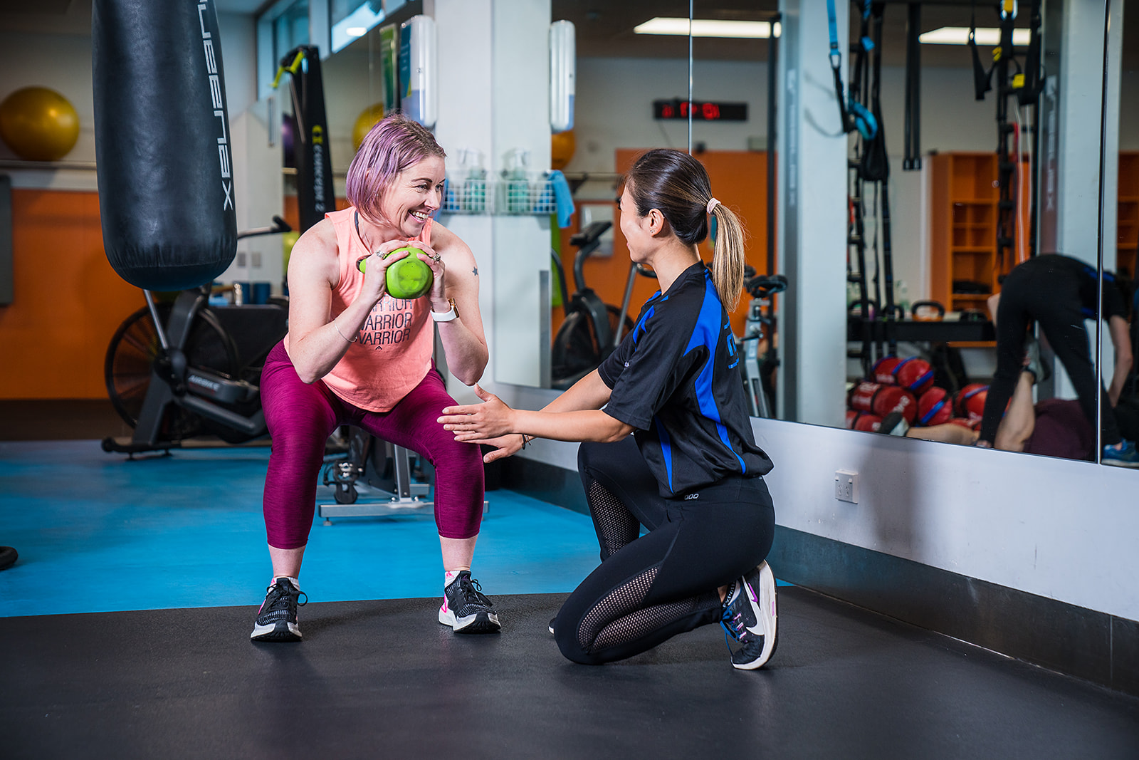 A female personal trainer assisting a woman in pink through a kettle bell workout at Christchurch Recreation and Sport Centre. 