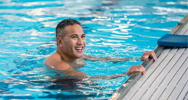 A smiling man holding onto the side of the pool at Christchurch Recreation and Sport pool.