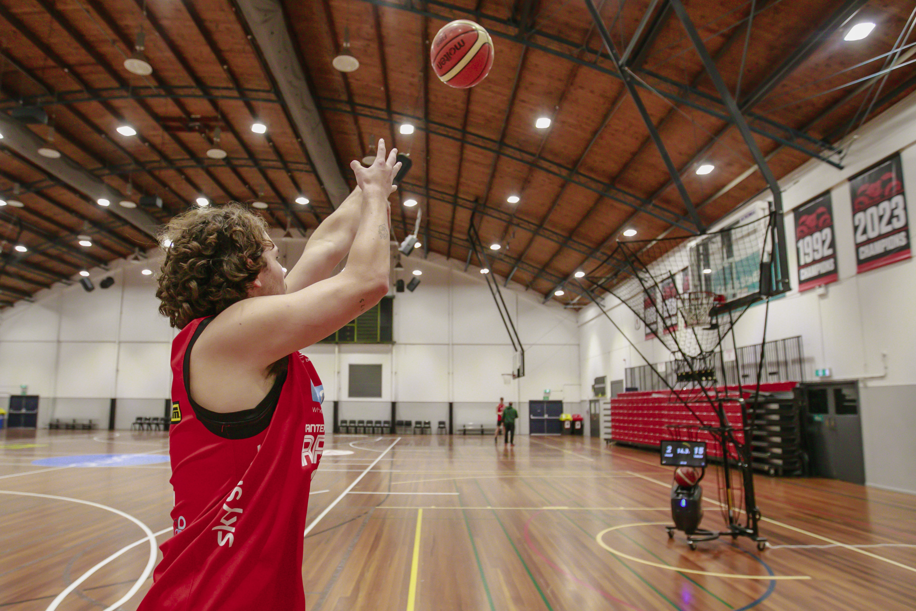 A Canterbury Rams player shooting at a basketball net using a basketball shooting machine at Christchurch Recreation and Sport. 