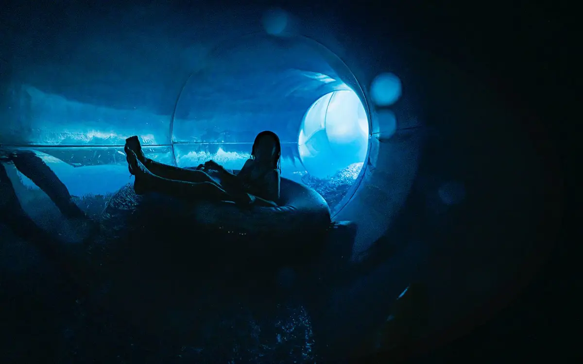 A child sliding down the blue hydroslide at QEll Recreation and Sport Centre in a blue ring raft.