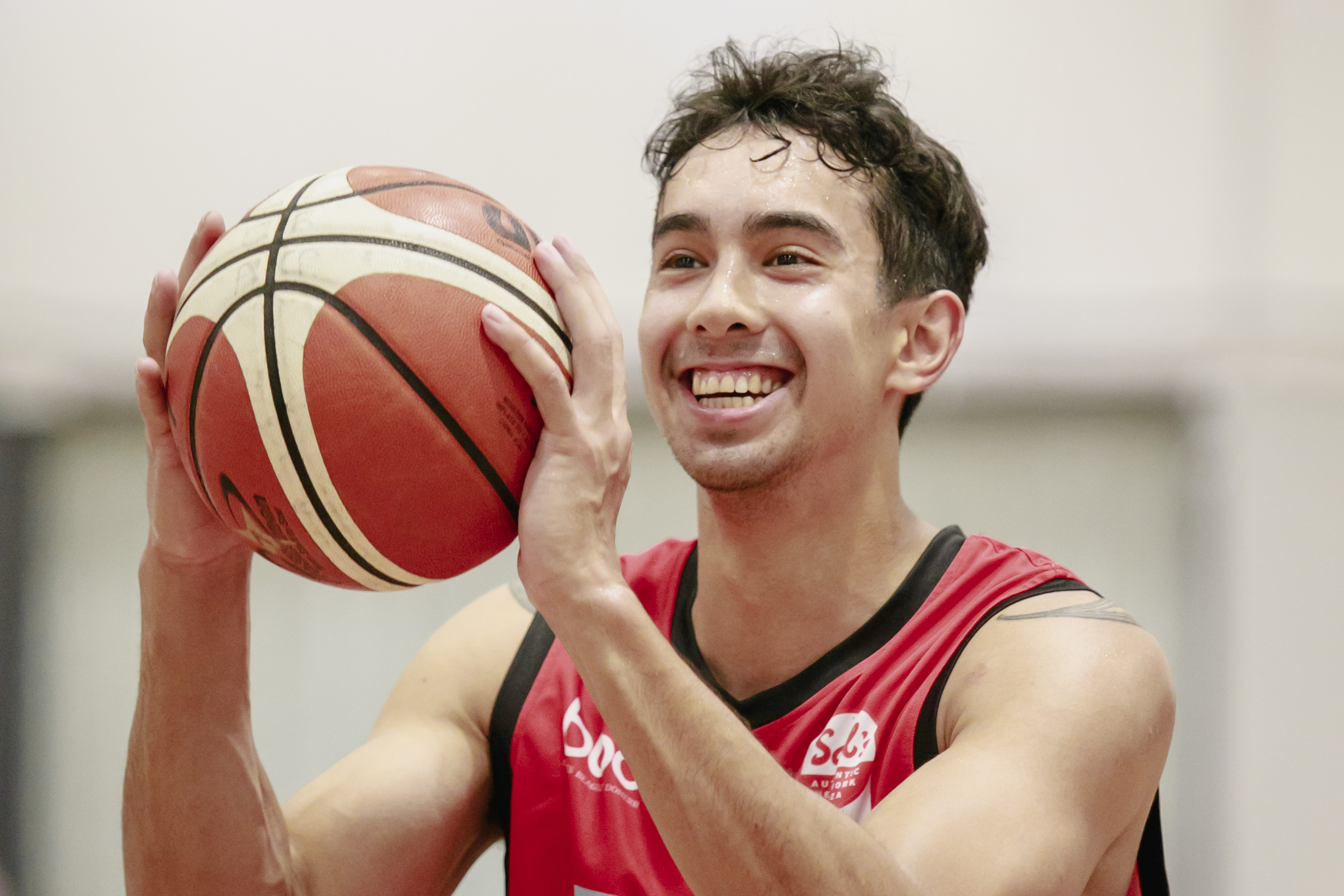 A smiling Canterbury Rams player shooting at a basketball net at Christchurch Recreation and Sport. 