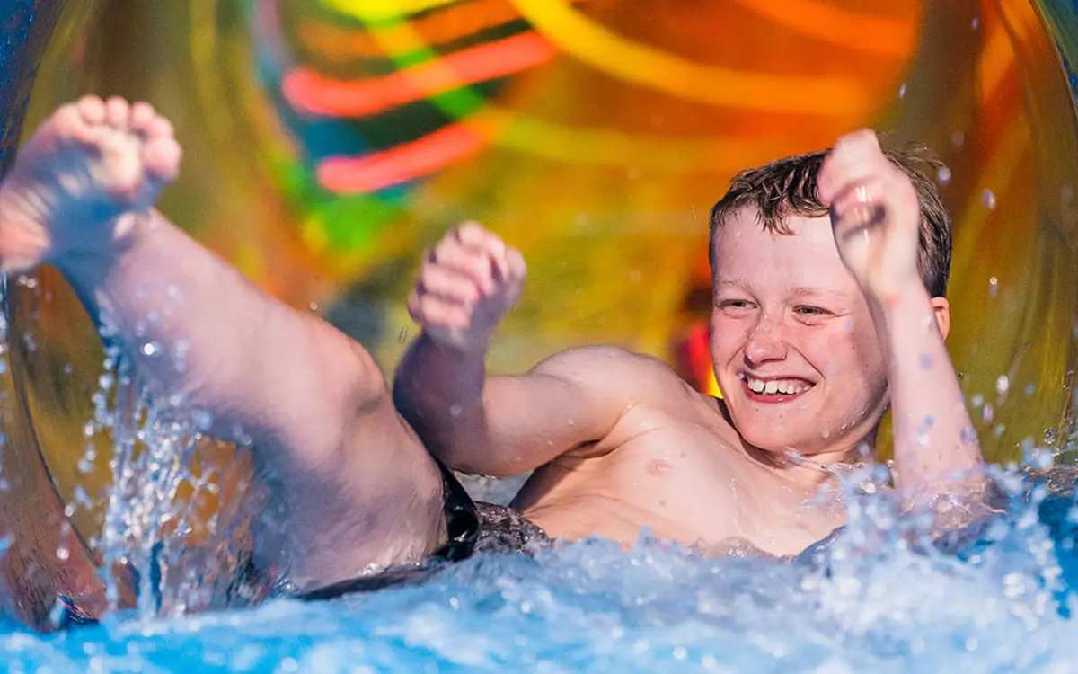 A smiling boy sliding down the hydroslide at Jellie Park outdoor pool.