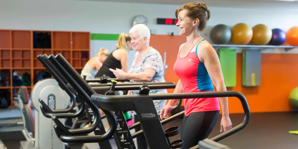 Two women walking and smiling on treadmills at Pioneer Rec and Sport Centre.