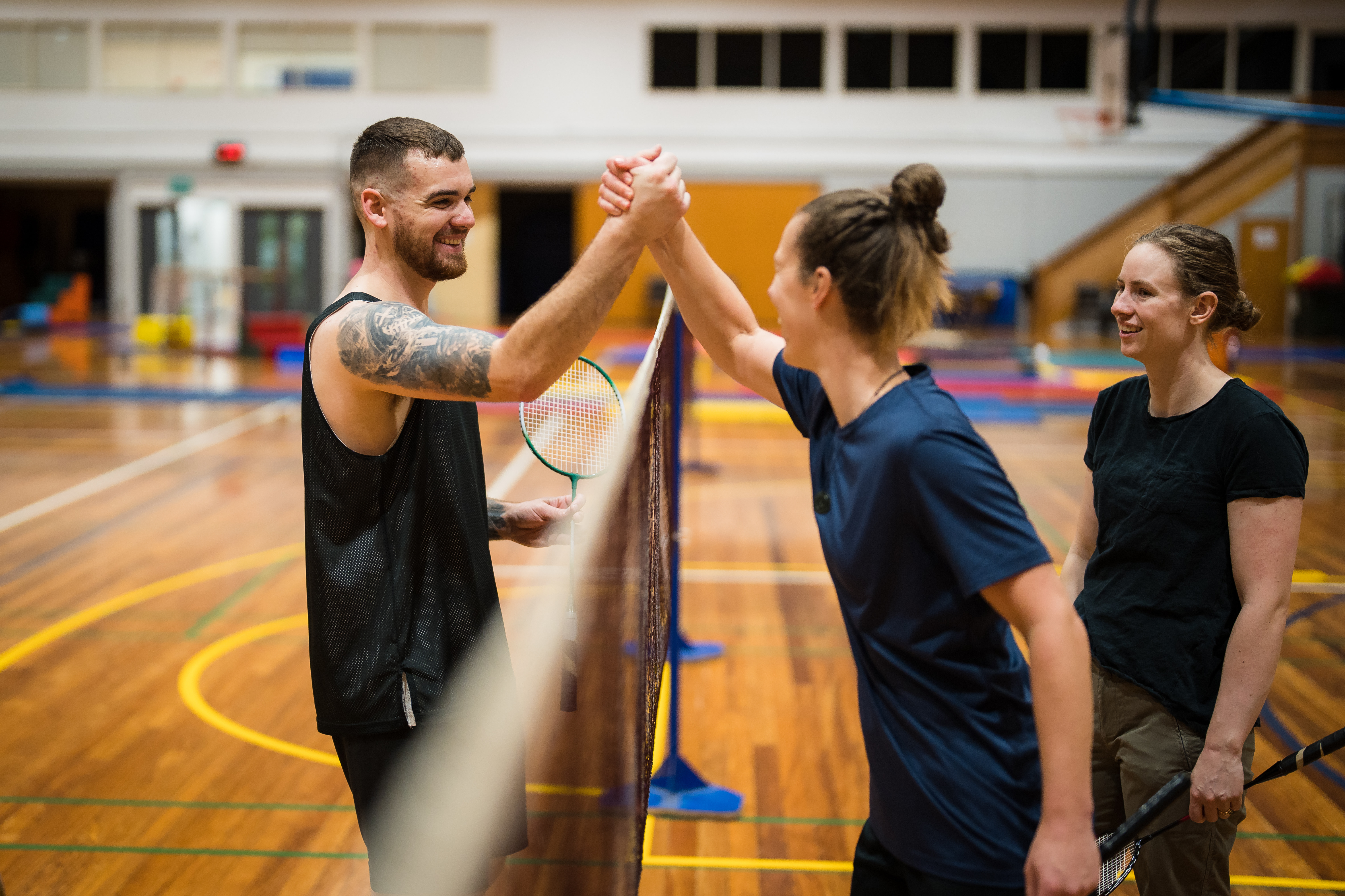 A man and a woman smiling while shaking hands after a badminton game at Christchurch Recreation and Sport. 