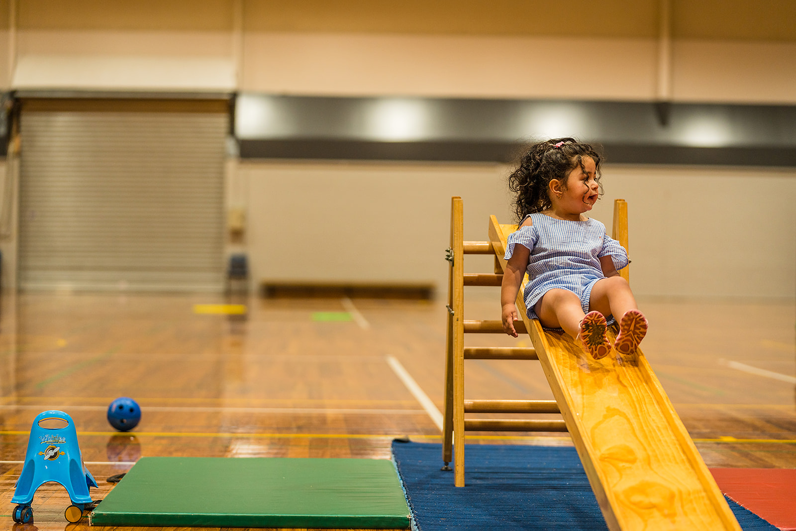 A smiling child sliding down a wooden slide during a Tumbletimes class at Christchurch Recreation and Sport Centre. 