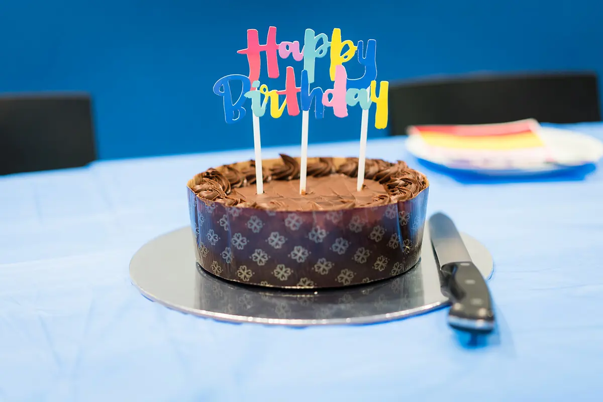 A chocolate cake with a Happy Birthday sign on the top. Sitting on a blue table.