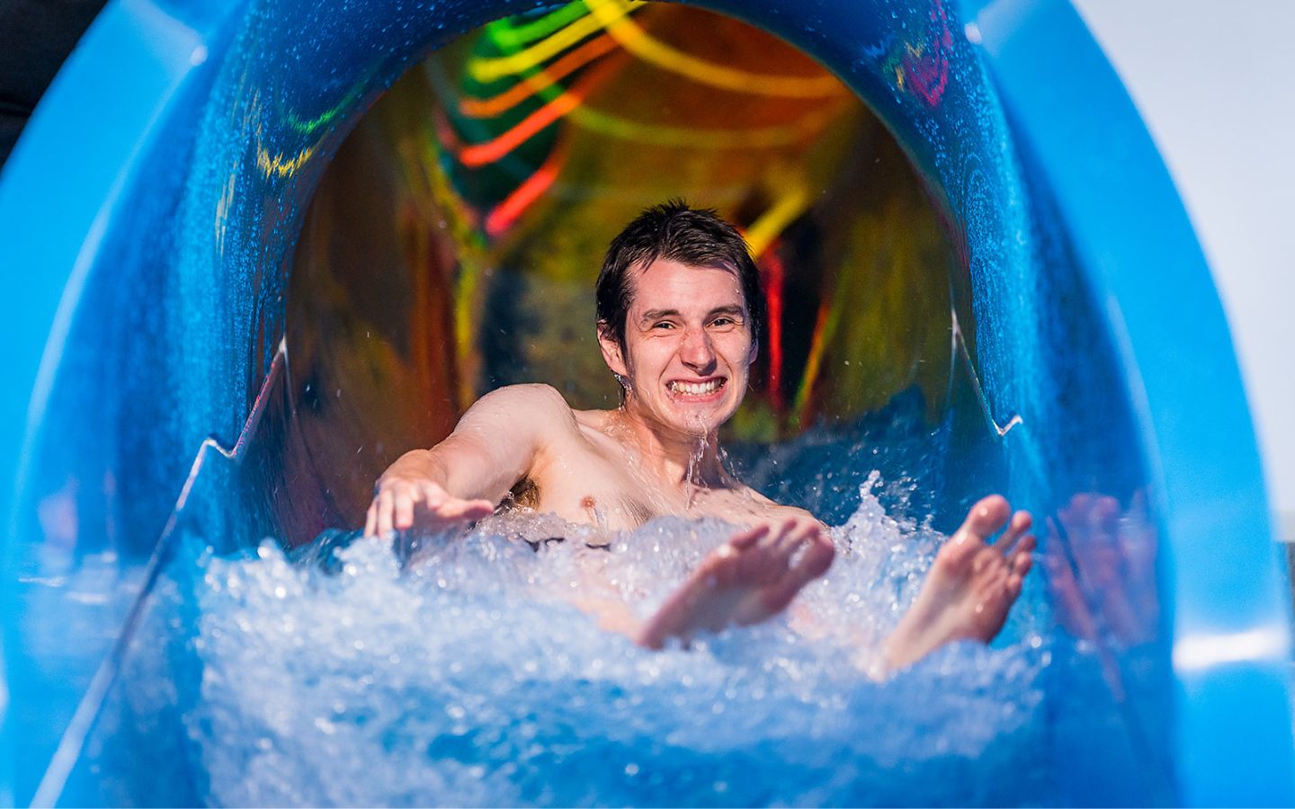 A smiling man sliding down the blue hydroslide at Jellie Park outdoor pool. 