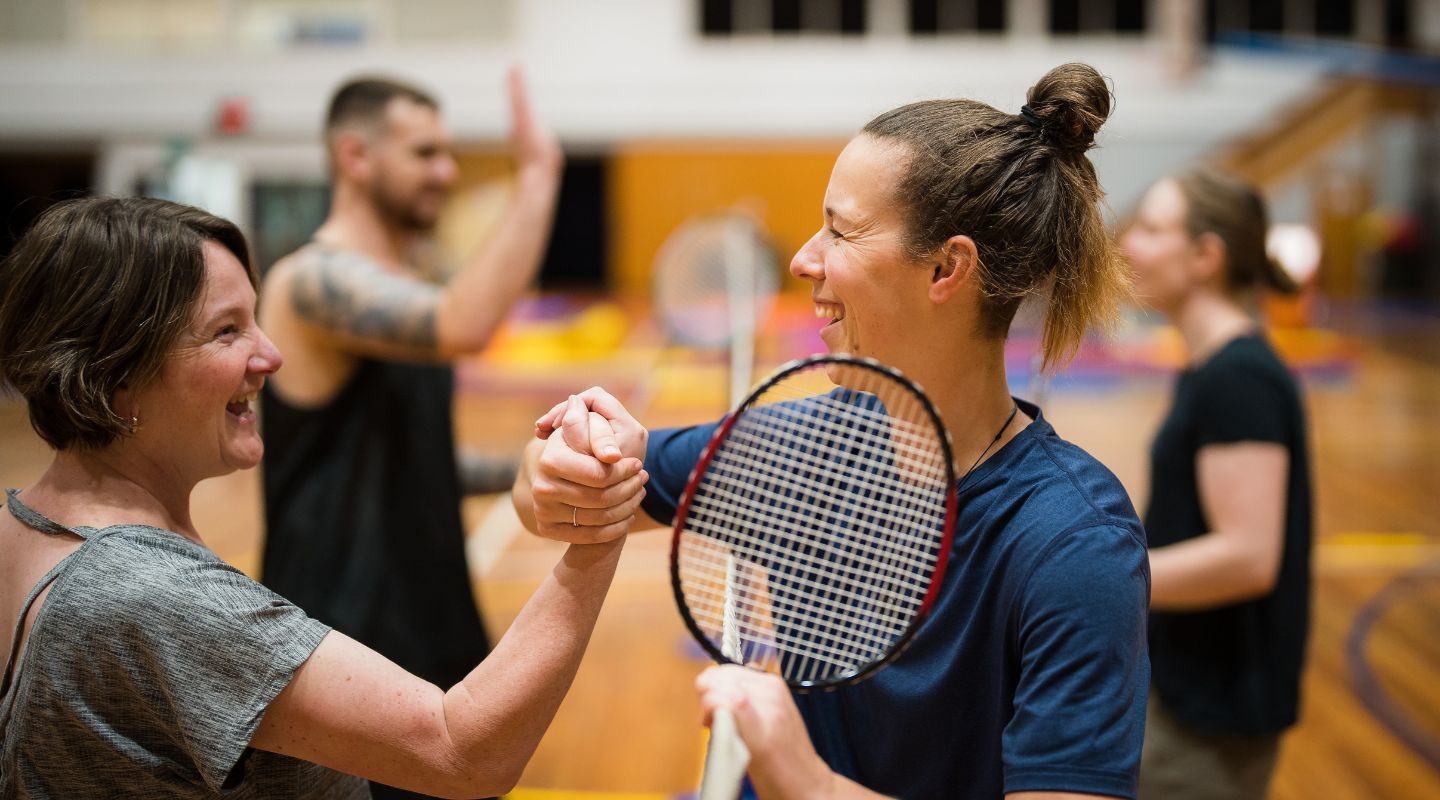 Four smiling people shaking hands after playing a doubles badminton game at Christchurch Recreation and Sport centre. 